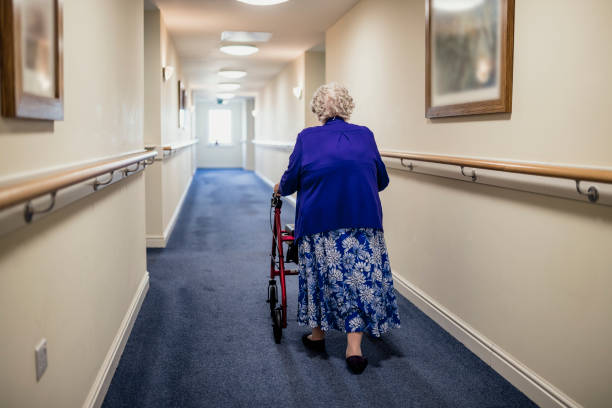 assisy A senior woman walking down a corridor with the assistance of a walker. view from rear