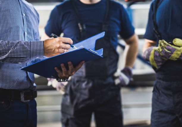 Unrecognizable owner going through reports with two workers in a warehouse. Unrecognizable owner going through reports with two workers in a warehouse.