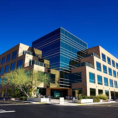 one comm build Stunning Scottsdale Arizona business building on blue backgrounded sky with matching blue glass windows beautifully landscaped with desert tolerant plant and trees on a clear day with set on a bright blue clear sky background.
