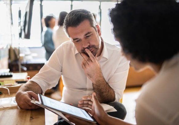 Mature man looking at a digital tablet that a colleague is showing at work Mature man looking at a digital tablet that a colleague is showing at work