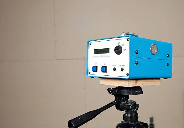 radon "A continuous radon monitor is mounted to a tripod in an unfinished house basement. A house is commonly tested for radon with a single use test kit. If initial readings are high or remediation work has begun a system like this would be used to determine a more accurate measurement over time. An added benefit of this unit is real time measurement. The display screen reads Avg. 3.5 pCi/l (picocuries per liter), the curie is a unit of radioactivity. The background is unfinished drywall with seams and screws."